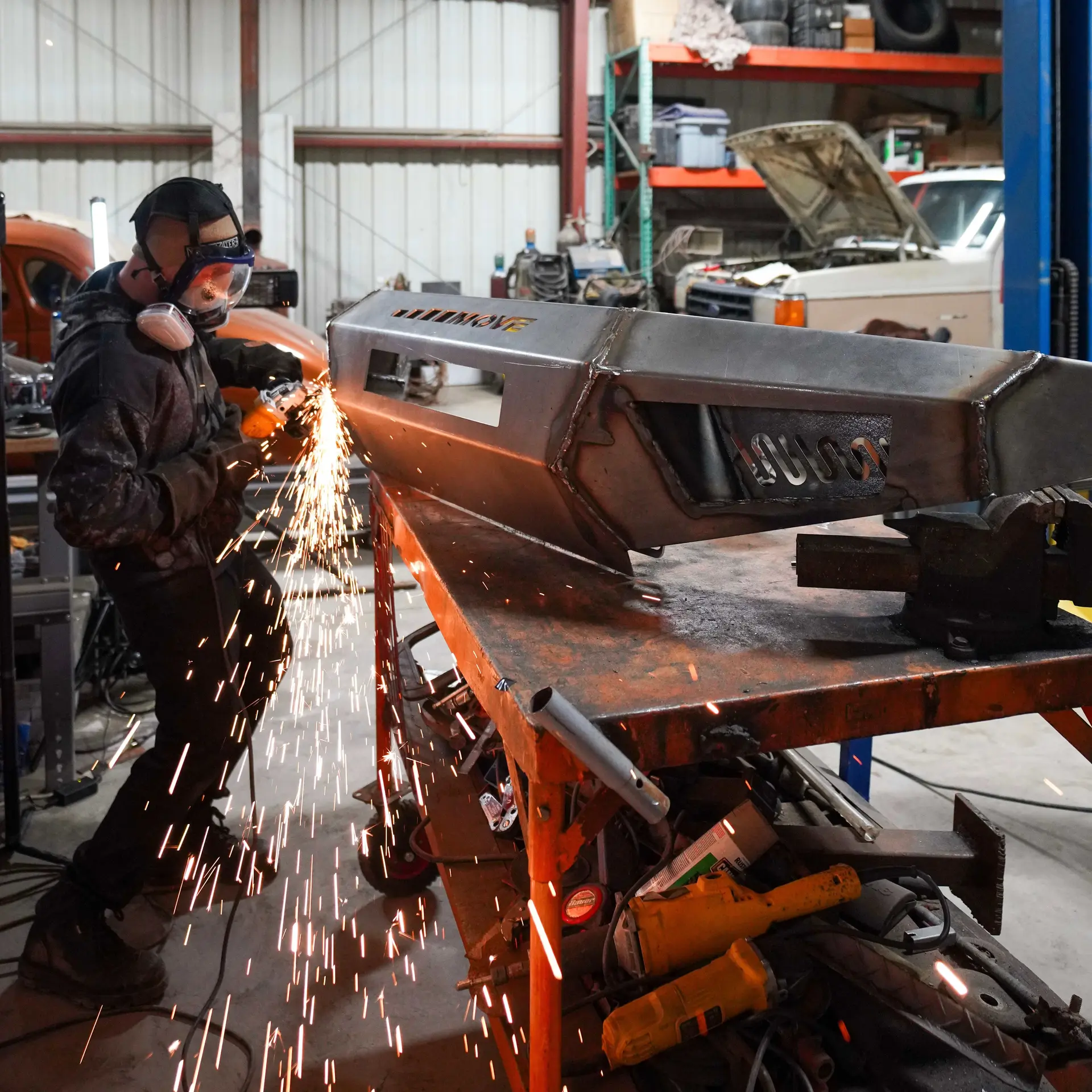 Fabricator in protective gear grinding a raw steel MOVE Bumpers bumper with sparks flying