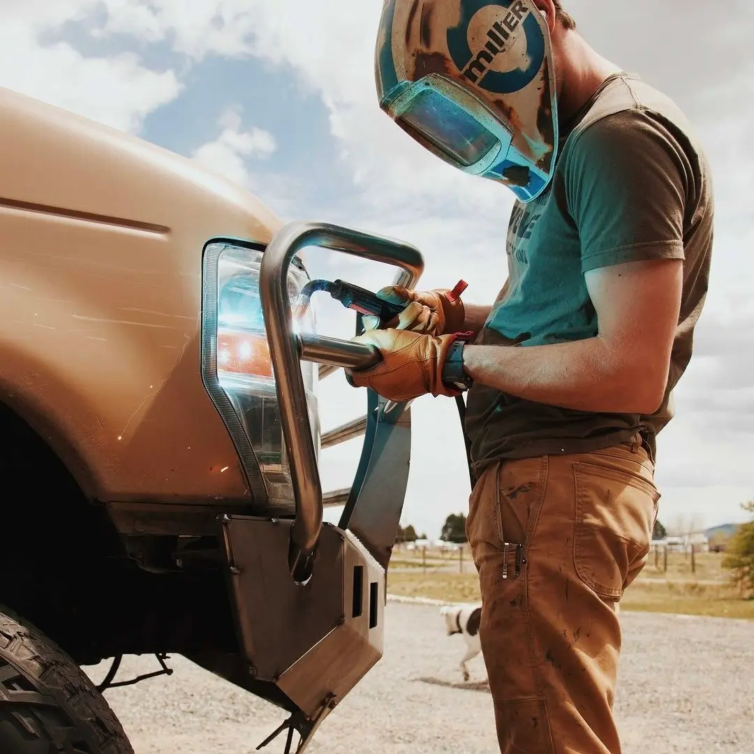 DIY builder welding a MOVE Bumpers bull bar onto a Ford truck outdoors in rural Montana